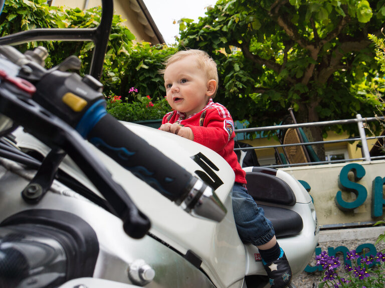 Ein Baby sitzt lächelnd auf dem Rücksitz eines Motorrads in der Nähe des Hotels Sponsel-Regus