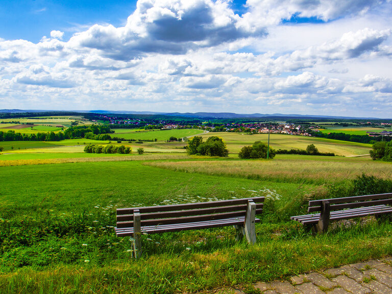 Eine Bank auf einer üppig grünen Wiese in einer ländlichen Gegend in der Fränkischen Schweiz
