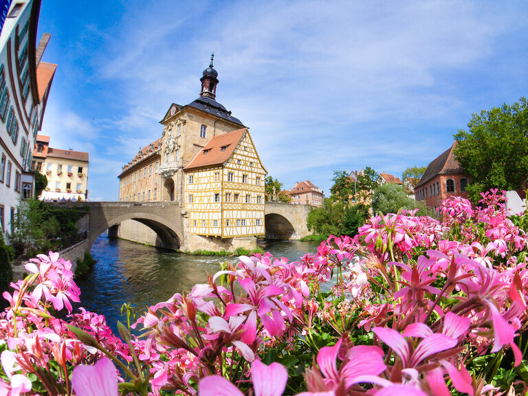 Eine Brücke über einen Fluss in Bamberg mit bunt blühenden Blumen im Vordergrund.