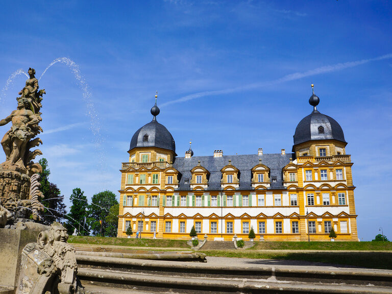 Das beeindruckende Schloss Seehof mit kunstvollen Details und einem Brunnen im Vordergrund.