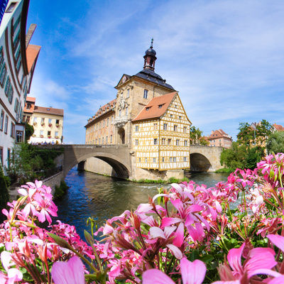 Eine Brücke über einen Fluss in Bamberg mit bunt blühenden Blumen im Vordergrund.