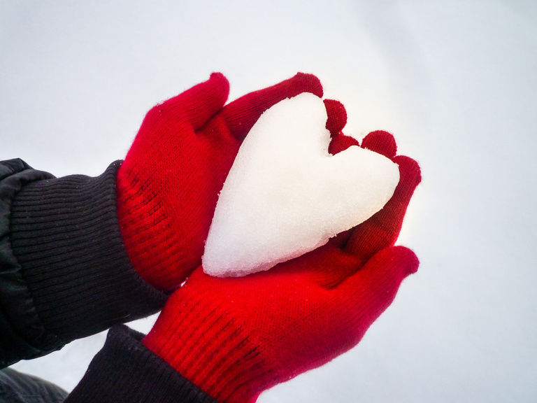 Hände mit roten Handschuhen halten ein Schneeherz