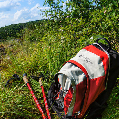 Ein Rucksack und zwei Wanderstöcke liegen auf einer grünen Wiese mit Blick auf die Natur der Fränkischen Schweiz