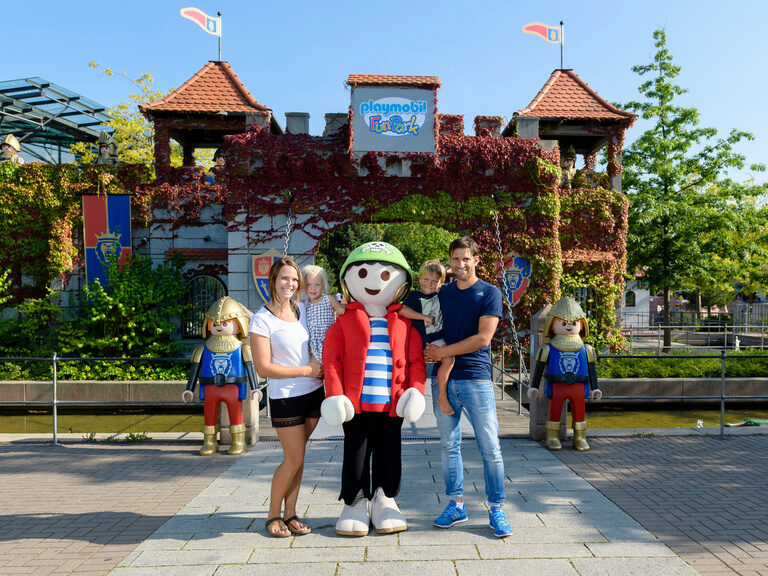 Eine Gruppe von Menschen posiert für ein Foto mit einer Playmobilfigur vor dem Playmobil-Funkpark