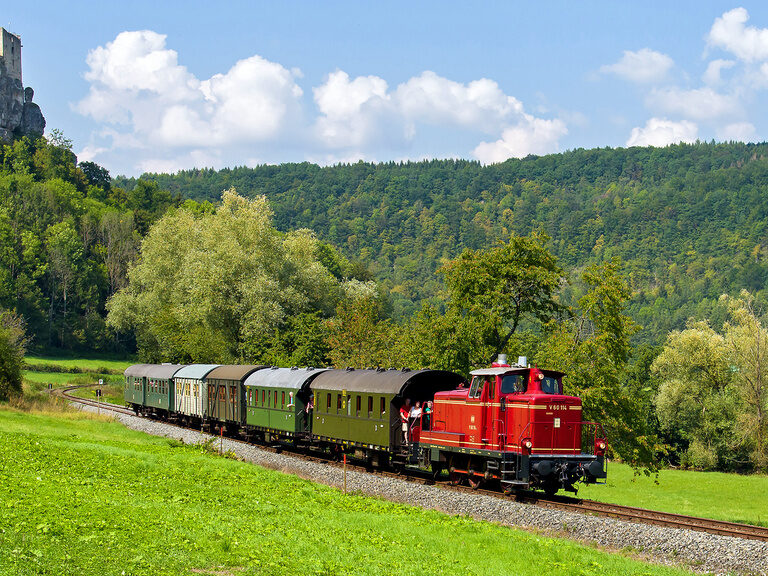 Der rote Zug der Dampfbahn Fränkische Schweiz fährt durch eine üppig grüne Landschaft.