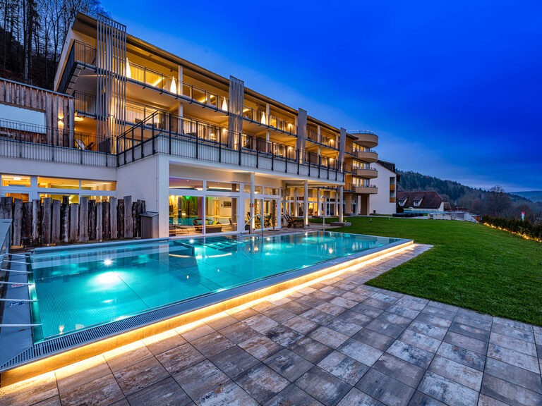 Außenansicht des Wellnesshotels Sponsel-Regus in Franken mit Außenpool und Hotelgebäude in der Abenddämmerung.