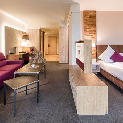 Eine violette Couch und ein luxuriöses Bett in der Turm-Familiensuite Schlössla in Franken.