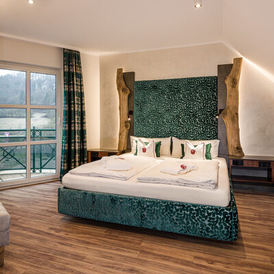 Ein großes Bett mit einem eleganten Holzrahmen in der geräumigen Komfort-Suite Mattstein
