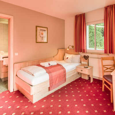 Ein komfortables Bett im Komfort-Einzelzimmer Stammhaus mit pinken Wänden und einem roten Teppich.