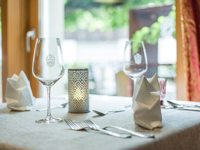 Ein Restaurant-Tisch im Landhaus Sponsel-Regus in Franken  ist mit stilvollem Geschirr und Weingläsern eingedeckt.