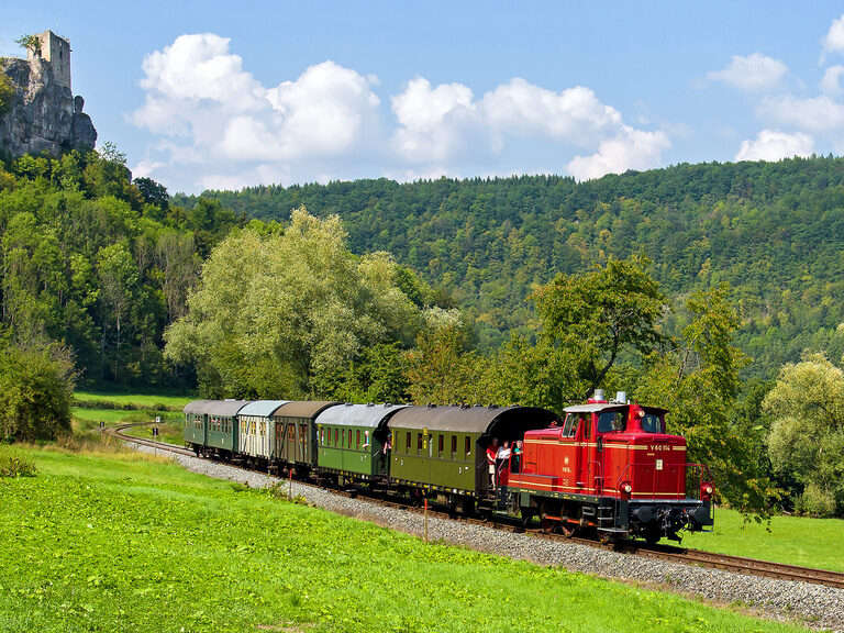 Der rote Zug der Dampfbahn Fränkische Schweiz fährt durch eine üppig grüne Landschaft.