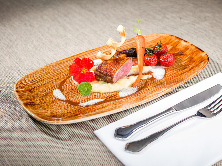 Ein Messer und eine Gabel liegen neben eine Teller mit einem besonders angerichteten Essen