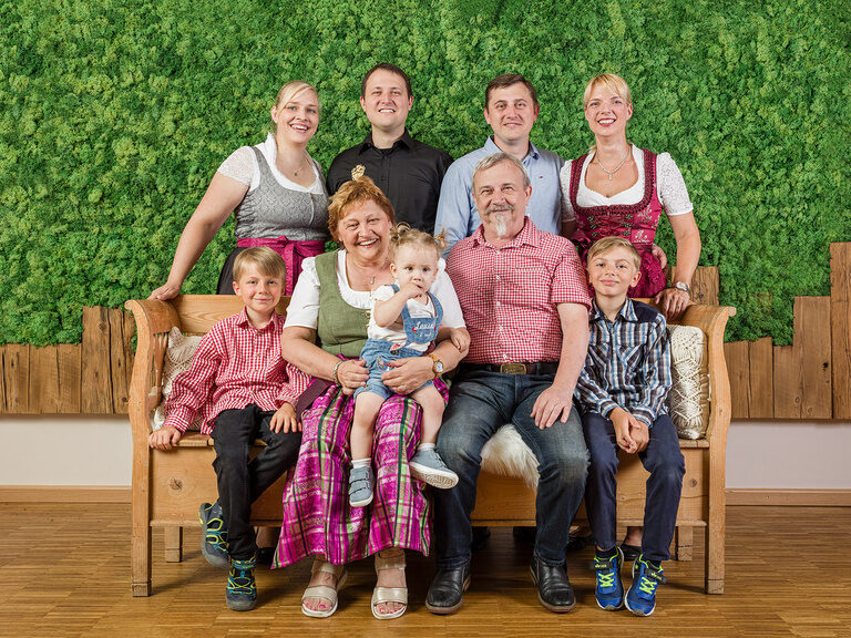 Die Gastgeberfamilie Regus sitzt auf einer Bank vor einer grünen Wand im Landhaus Sponsel-Regus