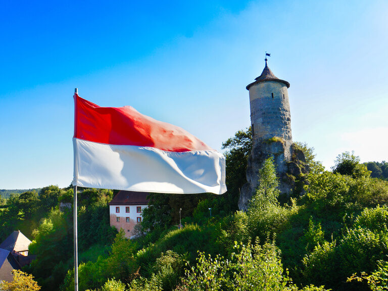 Die rot-weiße Flagge von Franken weht vor einem historischen Burgturm