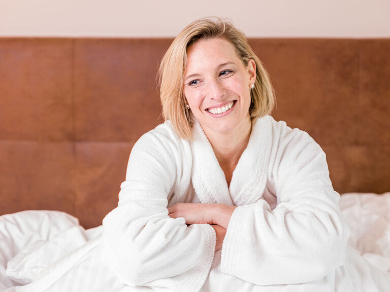 Eine Frau in einem weißen Bademantel entspannt auf einem Bett.