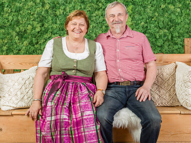 Das lächelnde Gastgeber-Ehepaar Regus sitzt auf einer Bank im Landhaus Sponsel-Regus.