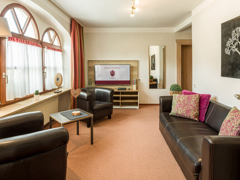 Ein komfortables Wohnzimmer mit großem Sofa und Sessel im Familienzimmer im Gästehaus.