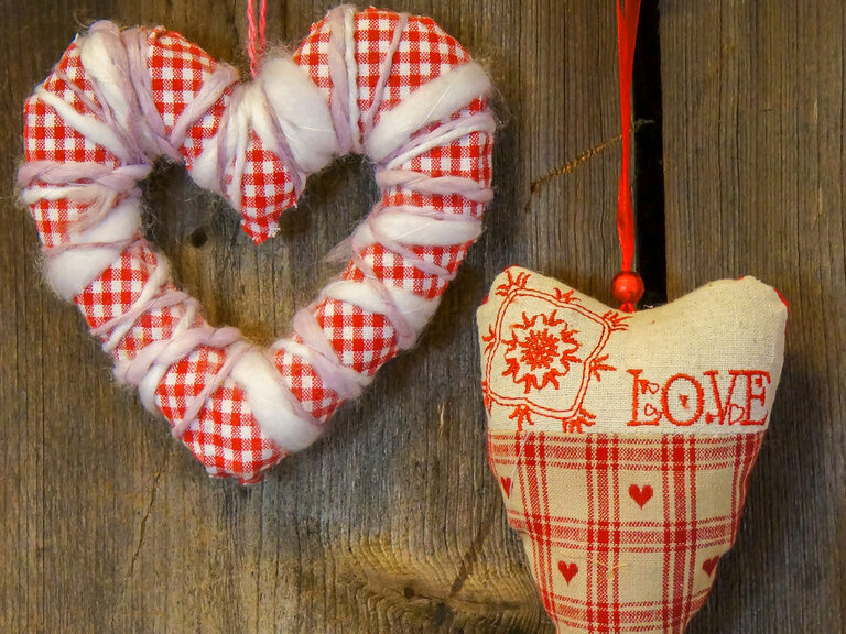 Romantische Herzen aus Stoff an einer Holzwand befestigt.