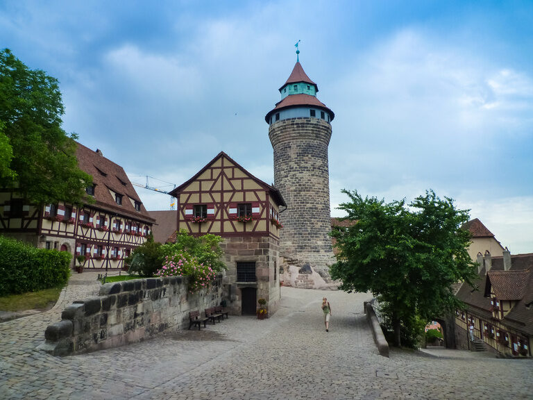 Ein altes Gebäude mit einem zentralen Turm erhebt sich majestätisch vor einem bewölkten Himmel.
