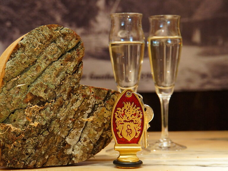 Ein aus Holz geschnitztes Herz steht mit zwei Gläsern Champagner auf einem Holztisch im Landhaus Sponsel-Regus