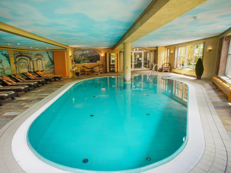 Ein eleganter Innenpool mit gemütlichen Liegestühlen und einem Wandgemälde im Wellnessbereich Mattstein des Hotels.