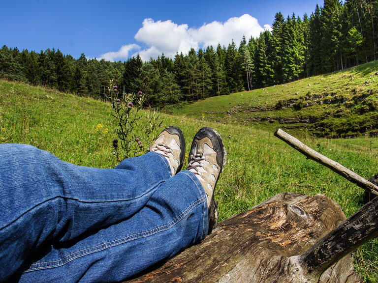 Eine Person legt in der grünen Landschaft der Fränkischen Schweiz die Füße hoch
