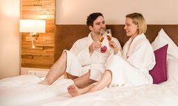 Ein Mann und eine Frau sitzen auf einem Bett und trinken Wein im Hotelzimmer - Landhaus Sponsel-Regus.