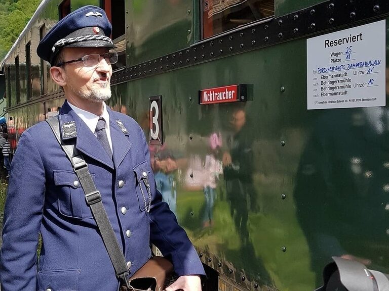 Der Lokführer in Uniform steht neben der Dampfbahn Fränkische Schweiz