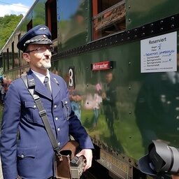 Der Lokführer in Uniform steht neben der Dampfbahn Fränkische Schweiz