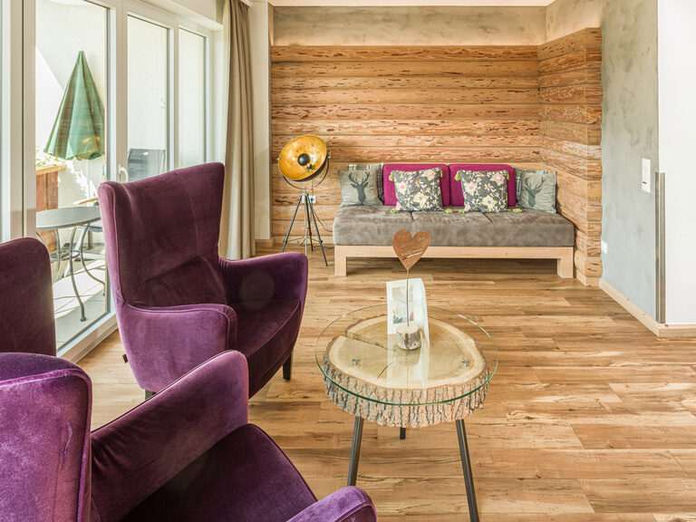 Das Wohnzimmer der Natur-Suite Schwalbennest bietet zwei lila Sessel und einen Couchtisch.