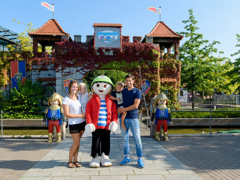 Eine Gruppe von Menschen posiert für ein Foto mit einer Playmobilfigur vor dem Playmobil-Funkpark