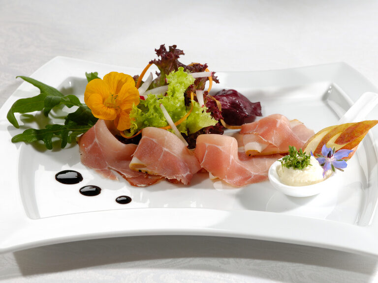 Ein kunstvoll angerichtetes Essen auf einem eleganten weißen Keramikteller im Restaurant des Hotels Sponsel-Regus