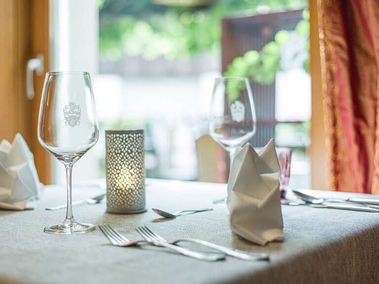 Ein Restaurant-Tisch im Landhaus Sponsel-Regus in Franken  ist mit stilvollem Geschirr und Weingläsern eingedeckt.