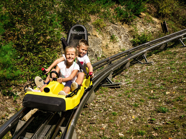 Zwei Kinder fahren mit der Rodelbahn der Erlebnismeile Pottenstein und haben Spaß
