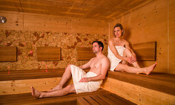 Ein Mann und eine Frau in Handtüchern bekleidet sitzen in einer Sauna des Hotels in Franken