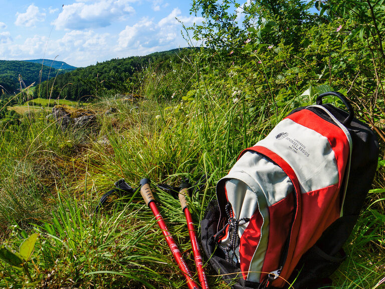 Ein Rucksack und zwei Wanderstöcke liegen auf einer grünen Wiese mit Blick auf die Natur der Fränkischen Schweiz