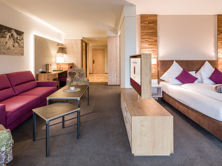 Eine violette Couch und ein luxuriöses Bett in der Turm-Familiensuite Schlössla in Franken.