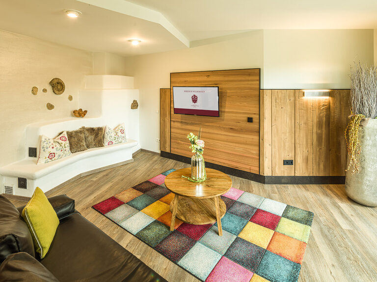 Eine Couch sowie ein bunter Teppich mit Holzboden in der hellen Suite Sonneck im Hotel Sponsel-Regus